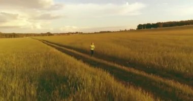 Sportif çocuk yeşil buğday tarlasında koşuyor. Kırsal çayırlarda akşam sporu alıştırmaları. Mutlu bir çocukluk sağlıklı bir yaşam biçimidir. Radikal hareket, güneş ışınları ve ot.