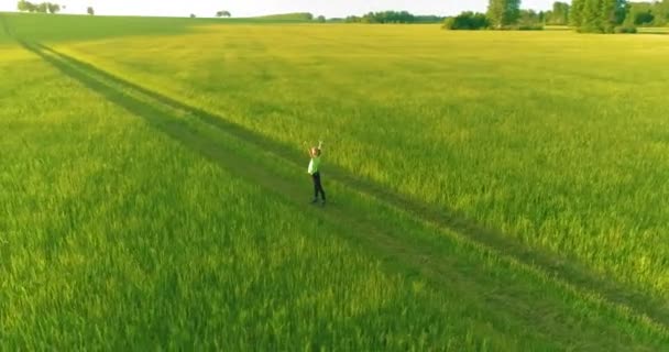 Спортивный ребенок стоит на зеленом пшеничном поле с поднятыми руками. Вечерние спортивные тренировки на сельском лугу. Счастливое детство это здоровый образ жизни. Радиальная панорама движения, солнечные лучи и — стоковое видео