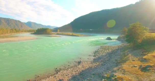 Vol à basse altitude au-dessus d'une rivière de montagne fraîche et rapide avec des rochers au soleil matin d'été. — Video