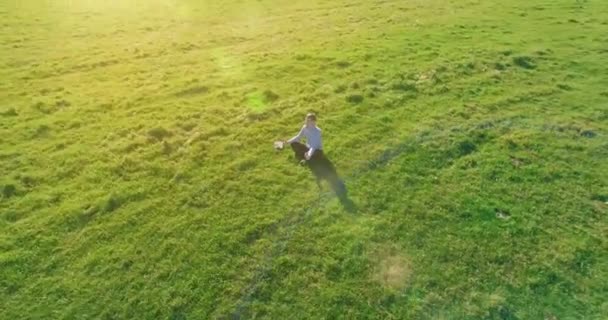 Niski lot orbitalny wokół człowieka na zielonej trawie z notatnikiem na żółtym polu wiejskim. — Wideo stockowe