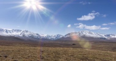 Güneş 'in kristal berrak gökyüzünde, kar dağının tepesindeki bulutlarla hareket zamanı. Sonbahar yüksek rakımlı çayırlarda sarı çimenler. Vahşi sonsuz doğa..