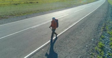 Asfalt yolda yürüyen otostopçu turist üzerinden uçuş. Yaz günü büyük bir kırsal vadi. Sırt çantalı gezgin..