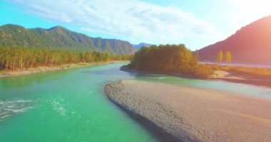 4k UHD hava görüntüsü. Güneşli yaz sabahında taze soğuk dağ nehri üzerinde alçak uçuş. Horisont 'ta yeşil ağaçlar ve güneş ışınları