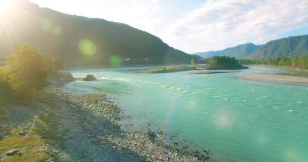 Vol à basse altitude au-dessus d'une rivière de montagne fraîche et rapide avec des rochers au soleil matin d'été. — Video