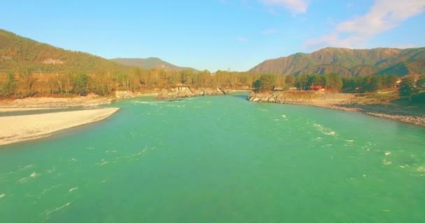 Vol à basse altitude au-dessus d'une rivière de montagne fraîche et rapide avec des rochers au soleil matin d'été. — Video