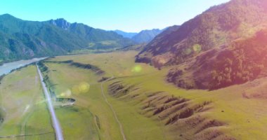 Güneşli yaz sabahında havadan kırsal dağ yolu ve çayır. Asfalt karayolu ve nehir.