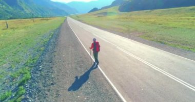 Asfalt yolda yürüyen otostopçu turist üzerinden uçuş. Yaz günü büyük bir kırsal vadi. Sırt çantalı gezgin..