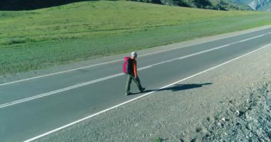 Asfalt yolda yürüyen otostopçu turist üzerinden uçuş. Yaz günü büyük bir kırsal vadi. Sırt çantalı gezgin..