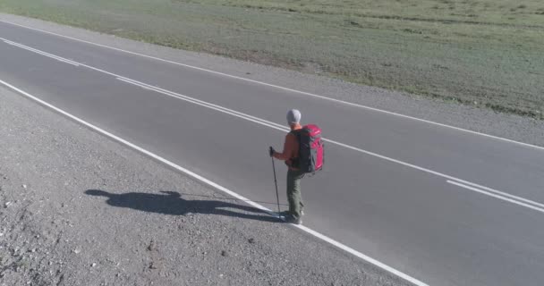 アスファルトの道路を歩くヒッチハイカーの観光客の上のフライト。夏の日に巨大な田舎の谷。リュックハイキング男. — ストック動画