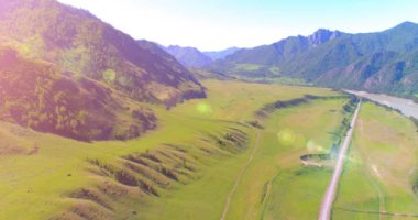 Güneşli yaz sabahında havadan kırsal dağ yolu ve çayır. Asfalt karayolu ve nehir.