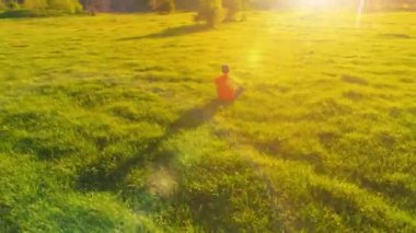 Yeşil çimlerde spor yogacısı üzerinde alçak irtifa radyal uçuş. Dağda gün batımı.