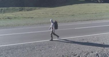 Asfalt yolda yürüyen otostopçu turist üzerinden uçuş. Yaz günü büyük bir kırsal vadi. Sırt çantalı gezgin..
