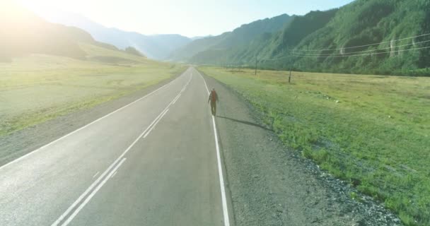 アスファルトの道路を歩くヒッチハイカーの観光客の上のフライト。夏の日に巨大な田舎の谷。リュックハイキング男. — ストック動画