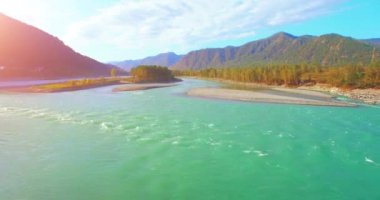 4k UHD hava görüntüsü. Güneşli yaz sabahında taze soğuk dağ nehri üzerinde alçak uçuş. Horisont 'ta yeşil ağaçlar ve güneş ışınları