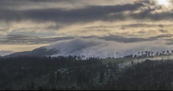 Timelapse of evening sun rays emerging through the cold foggy clouds in the mountains. Sunset in mountain fog. — Stock Video