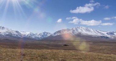 Güneş 'in kristal berrak gökyüzünde, kar dağının tepesindeki bulutlarla hareket zamanı. Sonbahar yüksek rakımlı çayırlarda sarı çimenler. Vahşi sonsuz doğa..