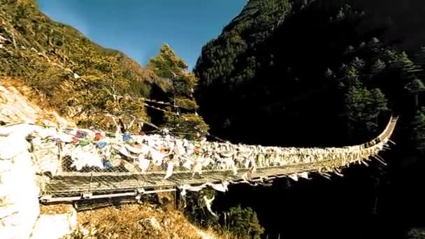 Maior ponte suspensa no vale de Khumbu com coloridas bandeiras de oração tibetanas. Himalaias selvagens natureza de alta altitude e monte vale. Encostas rochosas cobertas de árvores. Acampamento base da caminhada de pico do Everest. — Vídeo de Stock