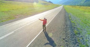 Asfalt yolda yürüyen otostopçu turist üzerinden uçuş. Yaz günü büyük bir kırsal vadi. Sırt çantalı gezgin..