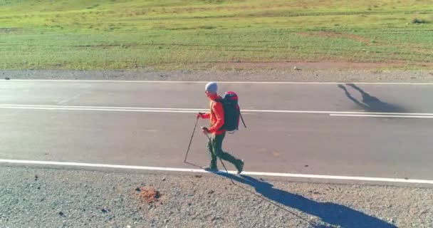 Voo sobre carona turista andando na estrada de asfalto. Vale rural enorme no dia de verão. Mochila caminhadas cara. — Vídeo de Stock