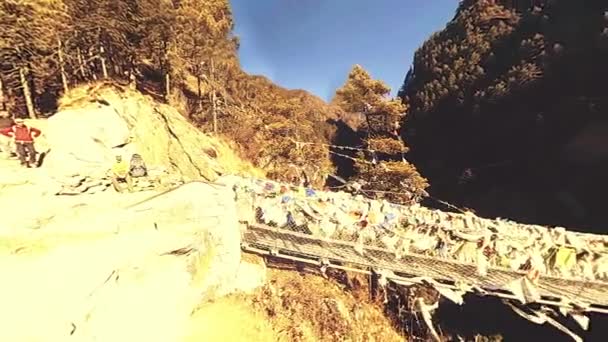 Största hängbron i Khumboudalen med färgglada tibetanska böneflaggor. Wild Himalaya hög höjd natur och berg dal. Klippiga sluttningar täckta med träd. Basläger av Everest topp vandring. — Stockvideo