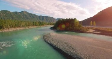 4k UHD hava görüntüsü. Güneşli yaz sabahında taze soğuk dağ nehri üzerinde alçak uçuş. Horisont 'ta yeşil ağaçlar ve güneş ışınları