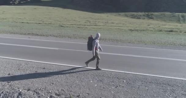 Vlucht over lifter toerist wandelen op asfalt weg. Enorme landelijke vallei op zomerdag. Rugzakwandelaar. — Stockvideo