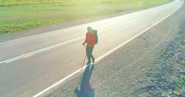 Volo sopra autostoppista turistico a piedi su strada asfaltata. Enorme valle rurale durante la giornata estiva. Zaino escursionista ragazzo. — Video Stock