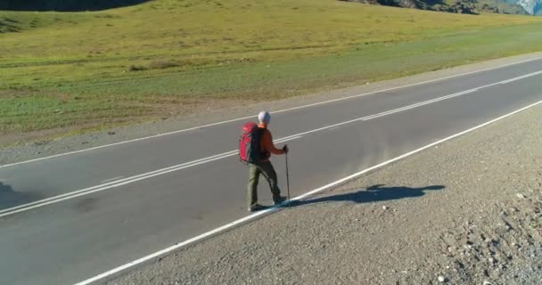 Vlucht over lifter toerist wandelen op asfalt weg. Enorme landelijke vallei op zomerdag. Rugzakwandelaar. — Stockvideo