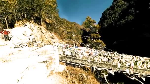 Größte Hängebrücke im Khumbu-Tal mit bunten tibetischen Gebetsfahnen. Wilde Himalaya-Hochgebirgsnatur und Bergtal. Felsige Hänge mit Bäumen bedeckt. Basislager des Everest-Gipfels. — Stockvideo