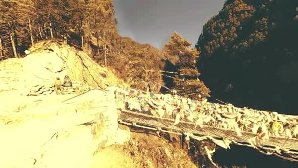 Grootste hangbrug in de Khumbu vallei met kleurrijke Tibetaanse gebedsvlaggen. Wild Himalaya 's hoge hoogte natuur en berg vallei. Rotsachtige hellingen bedekt met bomen. Basiskamp van de Everest piek trek. — Stockvideo