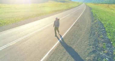 Asfalt yolda yürüyen otostopçu turist üzerinden uçuş. Yaz günü büyük bir kırsal vadi. Sırt çantalı gezgin..
