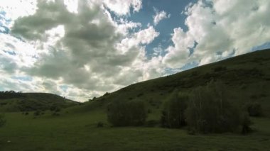 Yazın 4K UHD dağ çayırı zaman dilimi. Bulutlar, ağaçlar, yeşil çimenler ve güneş ışınları hareketi.