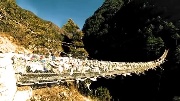 Найбільший висячий міст в долині Хумбу з барвистими тибетськими молитовними прапорами. Дикі Гімалаї височать над природою і долиною. Скелясті схили вкриті деревами. Піковий похід на Еверест.. — стокове відео