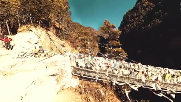 Largest suspension bridge in Khumbu valley with colorful Tibetan prayer flags. Wild Himalayas high altitude nature and mount valley. Rocky slopes covered with trees. Base camp of Everest peak trek. — Stock Video