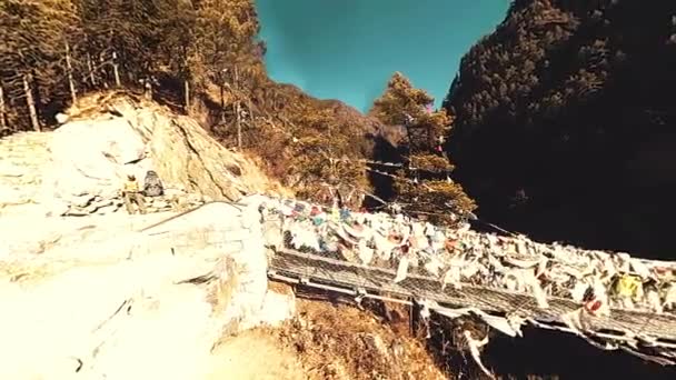 Största hängbron i Khumboudalen med färgglada tibetanska böneflaggor. Wild Himalaya hög höjd natur och berg dal. Klippiga sluttningar täckta med träd. Basläger av Everest topp vandring. — Stockvideo