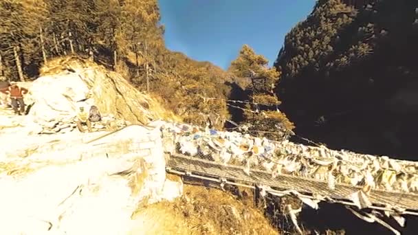 Größte Hängebrücke im Khumbu-Tal mit bunten tibetischen Gebetsfahnen. Wilde Himalaya-Hochgebirgsnatur und Bergtal. Felsige Hänge mit Bäumen bedeckt. Basislager des Everest-Gipfels. — Stockvideo