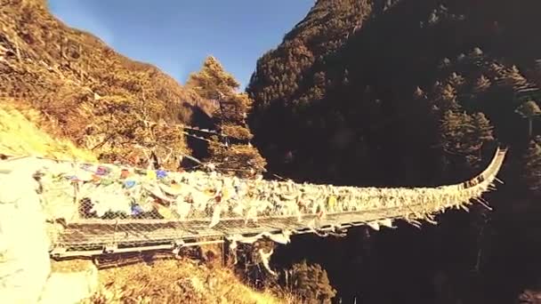 Largest suspension bridge in Khumbu valley with colorful Tibetan prayer flags. Wild Himalayas high altitude nature and mount valley. Rocky slopes covered with trees. Base camp of Everest peak trek. — Stock Video