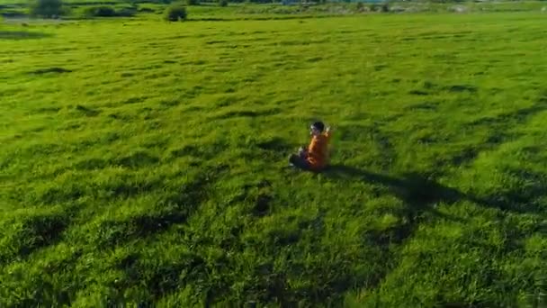 完璧な緑の芝生でスポーツヨガの男の上に低高度放射線飛行。山の夕日. — ストック動画