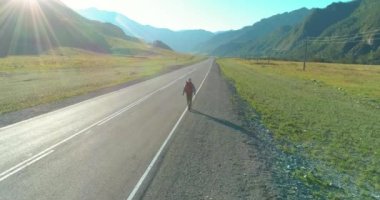 Asfalt yolda yürüyen otostopçu turist üzerinden uçuş. Yaz günü büyük bir kırsal vadi. Sırt çantalı gezgin..