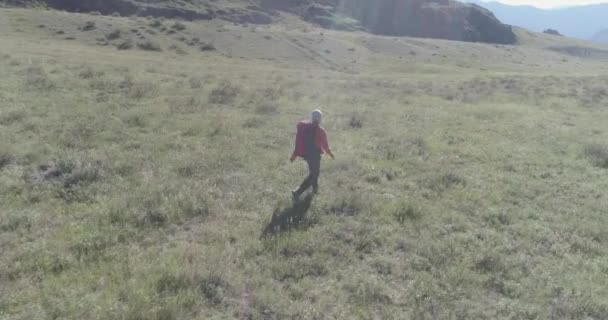 Vuelo sobre mochila senderismo turista caminando a través de campo de montaña verde. Gran valle rural en el día de verano. — Vídeos de Stock