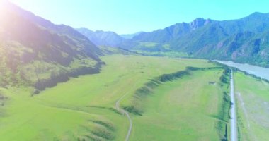 Güneşli yaz sabahında havadan kırsal dağ yolu ve çayır. Asfalt karayolu ve nehir.