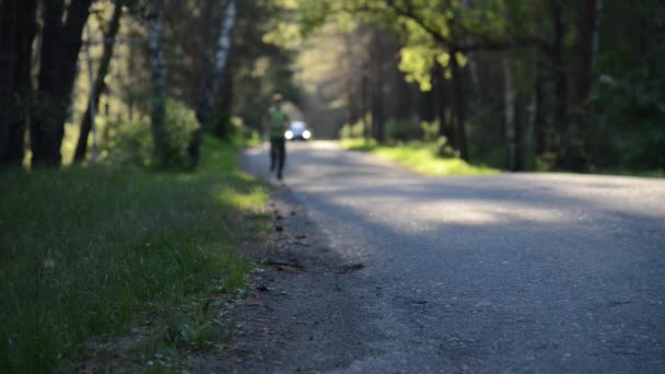 Sport man som springer på asfalterad väg. Landsbygdspark. Gröna träd skog och solstrålar vid horisonten. — Stockvideo