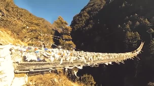 Größte Hängebrücke im Khumbu-Tal mit bunten tibetischen Gebetsfahnen. Wilde Himalaya-Hochgebirgsnatur und Bergtal. Felsige Hänge mit Bäumen bedeckt. Basislager des Everest-Gipfels. — Stockvideo