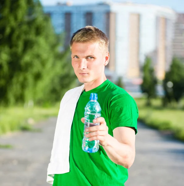 Trött man med vit handduk dricksvatten från en plastflaska — Stockfoto