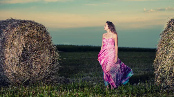 Woman standing in evening field over haystack. — Stock Photo, Image