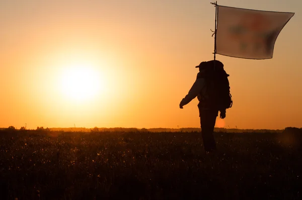 Турист с рюкзаком и флагом прогуливается по полю — стоковое фото