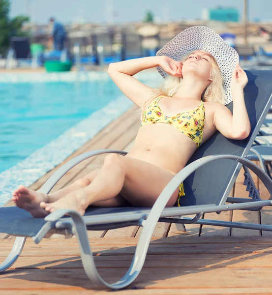 Ung kvinna i baddräkt som ligger på schäslong vid poolen — Stockfoto