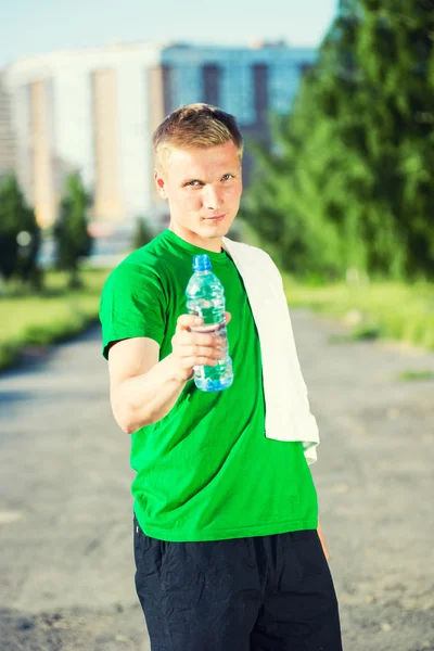 Tired man with white towel drinking water from a plastic bottle — Stock Photo, Image