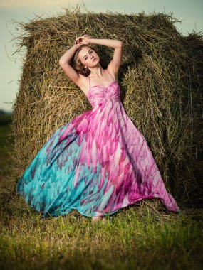 Akşam alanında haystack üzerinde duran genç kadın. Moda arpacık