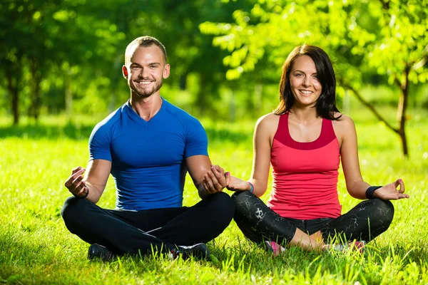 Hombre y mujer jóvenes haciendo yoga en el soleado parque de verano —  Fotos de Stock